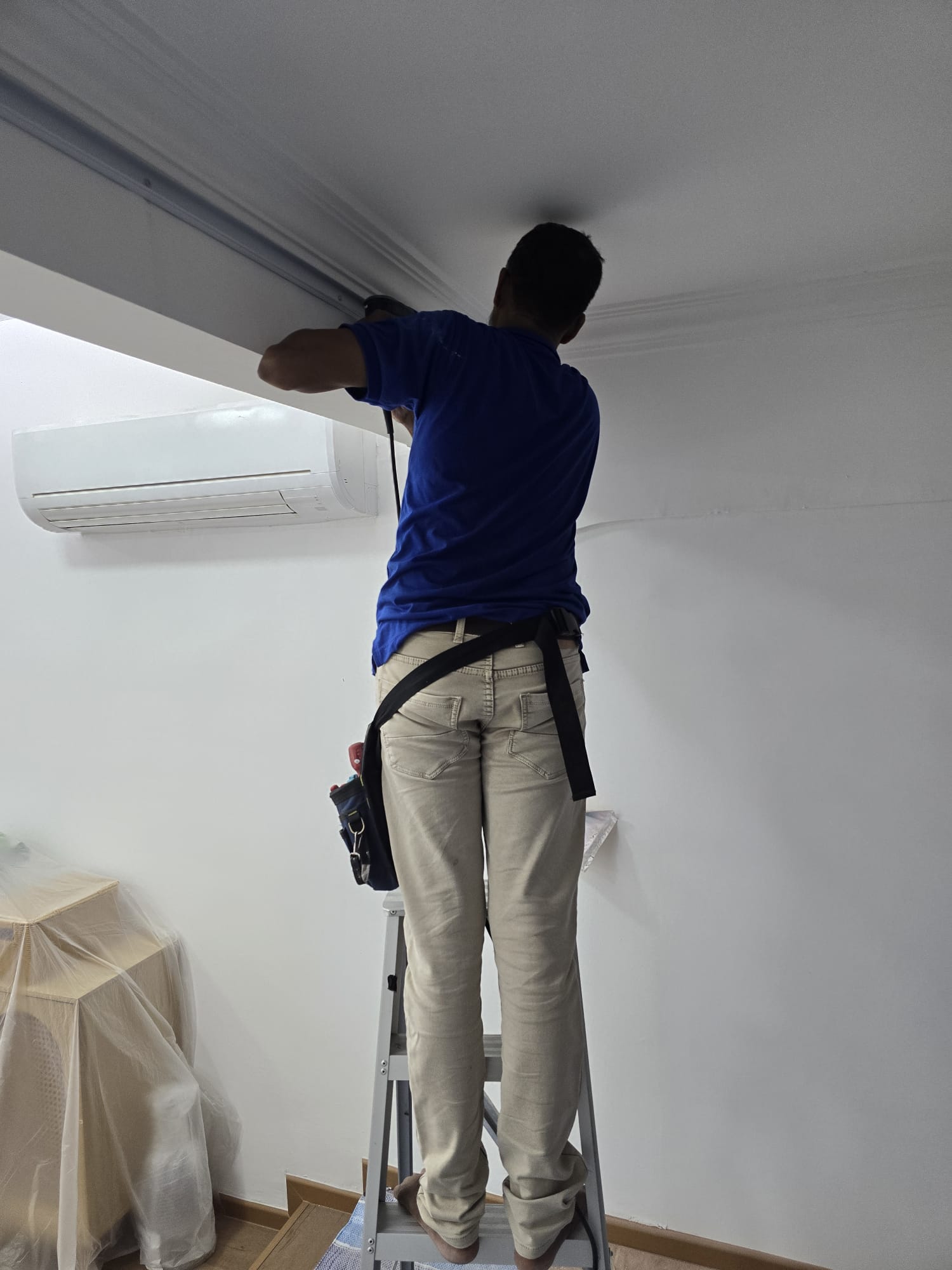 Electrician running trunking above an air-conditioner unit
